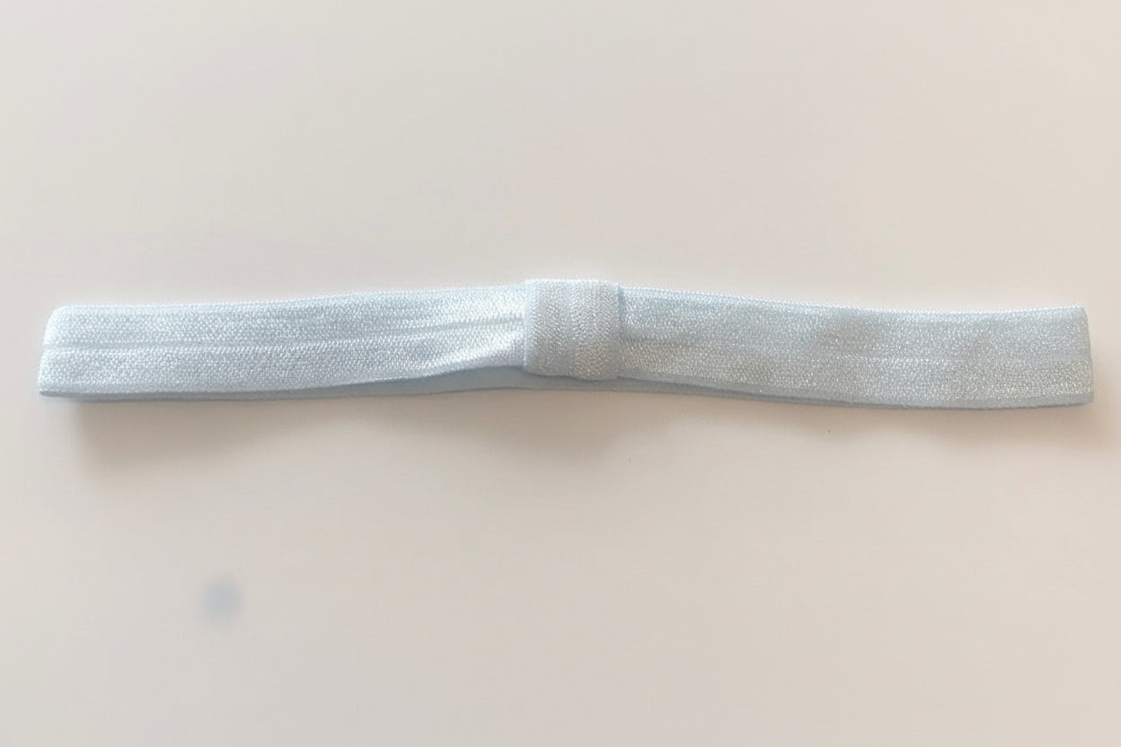 A blue elasticated baby headband designed to fit any size, with a small bow hair clip attached.